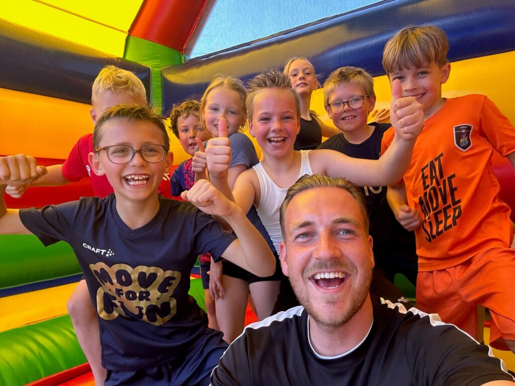 Kinderen op het springkussen met trainer Mats tijdens een sportieve sport en spel dag