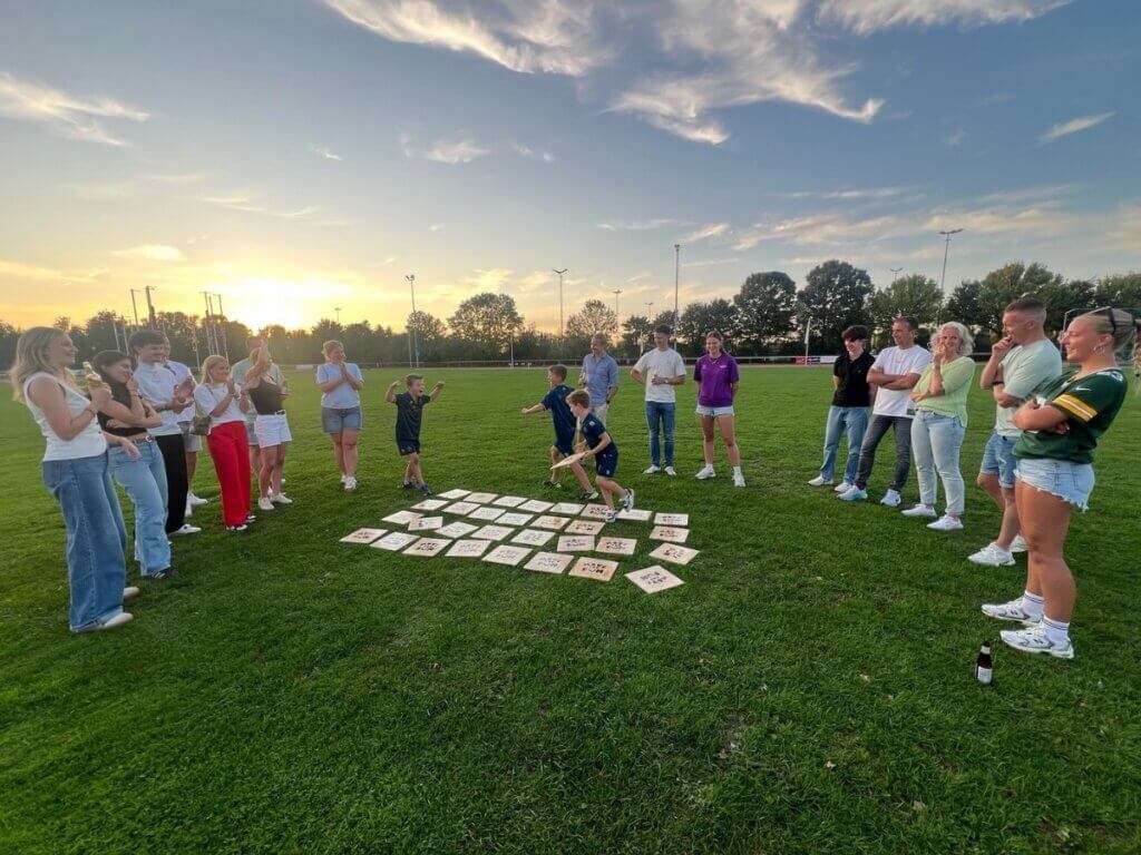 Groep volwassenen en kinderen speelt een gezelschapsspel tijdens zonsondergang op een zomerfeest van Move for Fun.