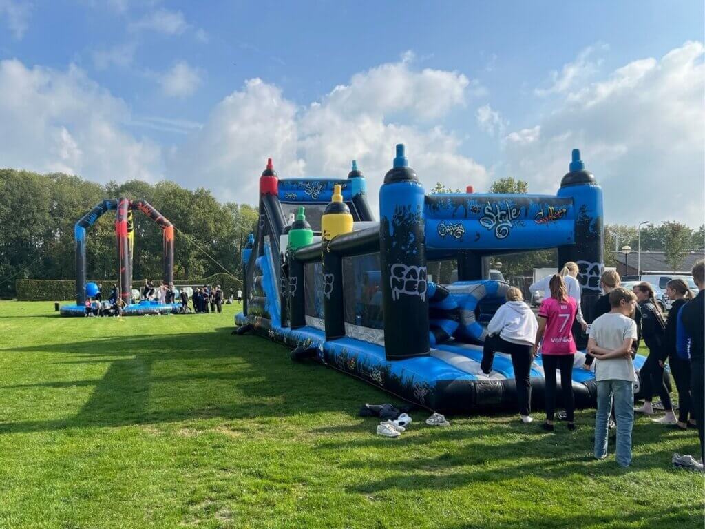 Deelnemers doen mee aan een actief spel op een groot opblaasbaar parcours tijdens een introductiedag van Move For Fun, gericht op samenwerking en plezier.
