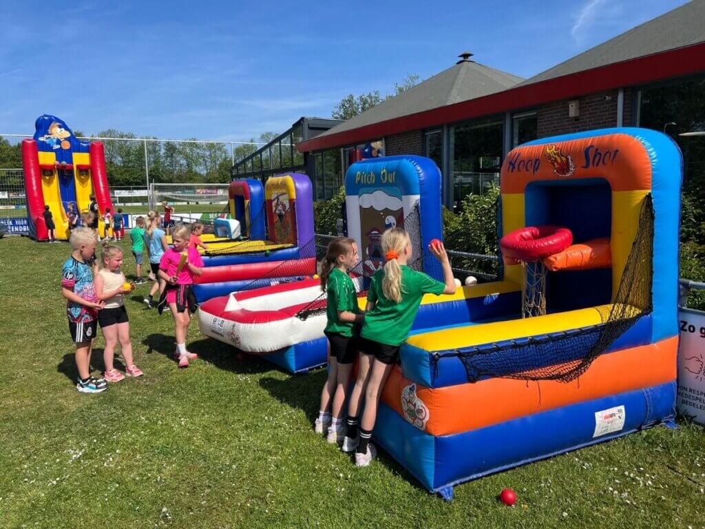 Kinderen spelen en voetballen op een grasveld tijdens het zomerfeest van Move for Fun, vol plezier en sportieve energie.