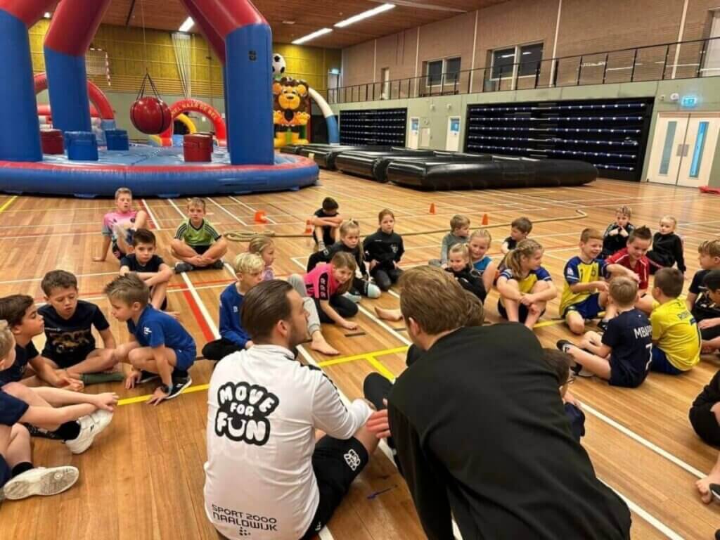 Kinderen doen mee aan een sportieve activiteit tijdens een schoolreisje op maat van Move For Fun met begeleiding in een sporthal vol opblaasbare attracties