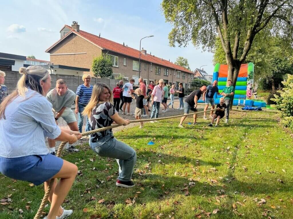 Volwassenen en kinderen doen enthousiast mee aan touwtrekken tijdens een zomerfeest van Move for Fun