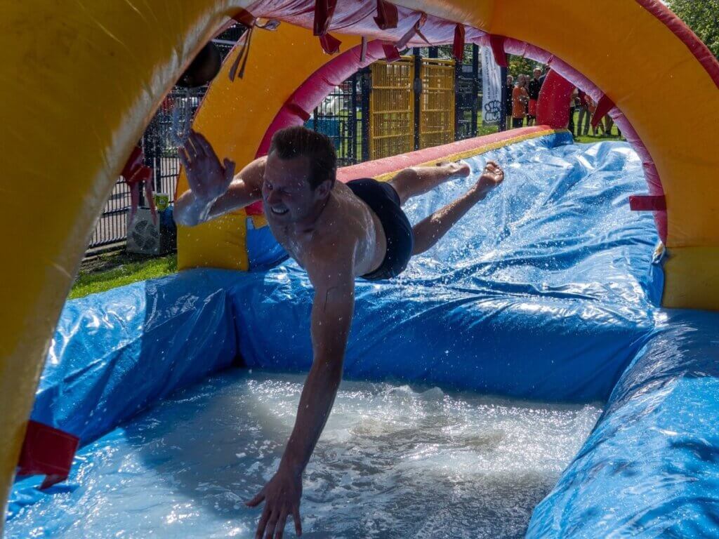 Man glijdt lachend over een waterbaan tijdens een zomerfeest georganiseerd door Move for Fun.