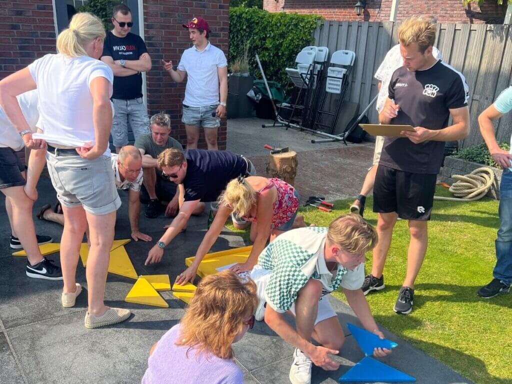 Een groep mensen lost samen een grote puzzel op in de tuin onder begeleiding van Move For Fun.