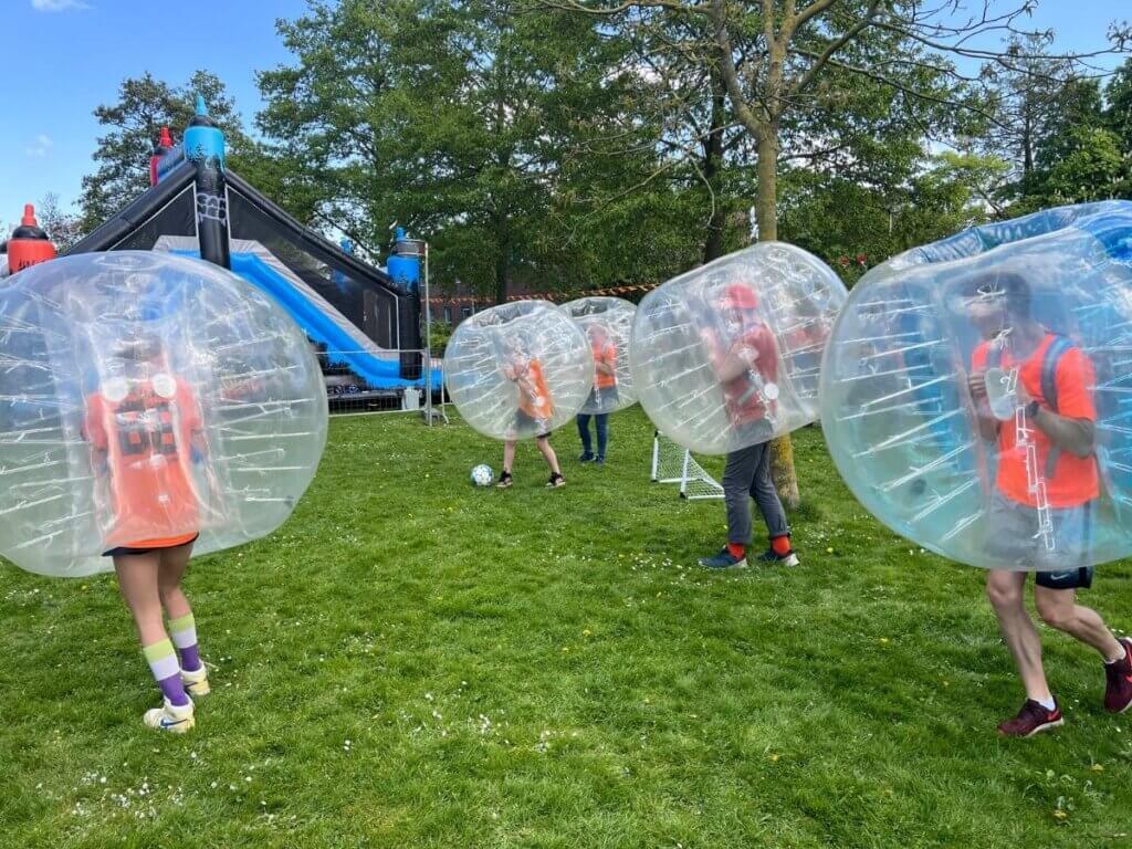 Deelnemers in grote opblaasbare bubbelpakken spelen bubble voetbal op een grasveld tijdens Koningsdag.