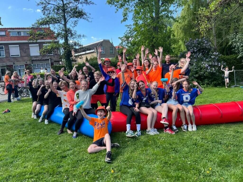 Grote groep deelnemers in oranje en sportkleding die lachend poseert voor een groepsfoto tijdens een Koningsdag evenement.