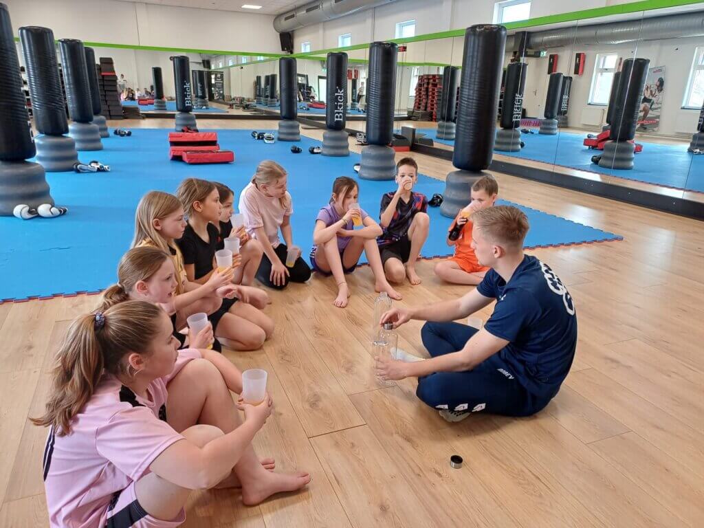 Kinderen zitten in een sportzaal en drinken wat tijdens een pauze van het kickboks kinderfeestje van Move For Fun in Westland.