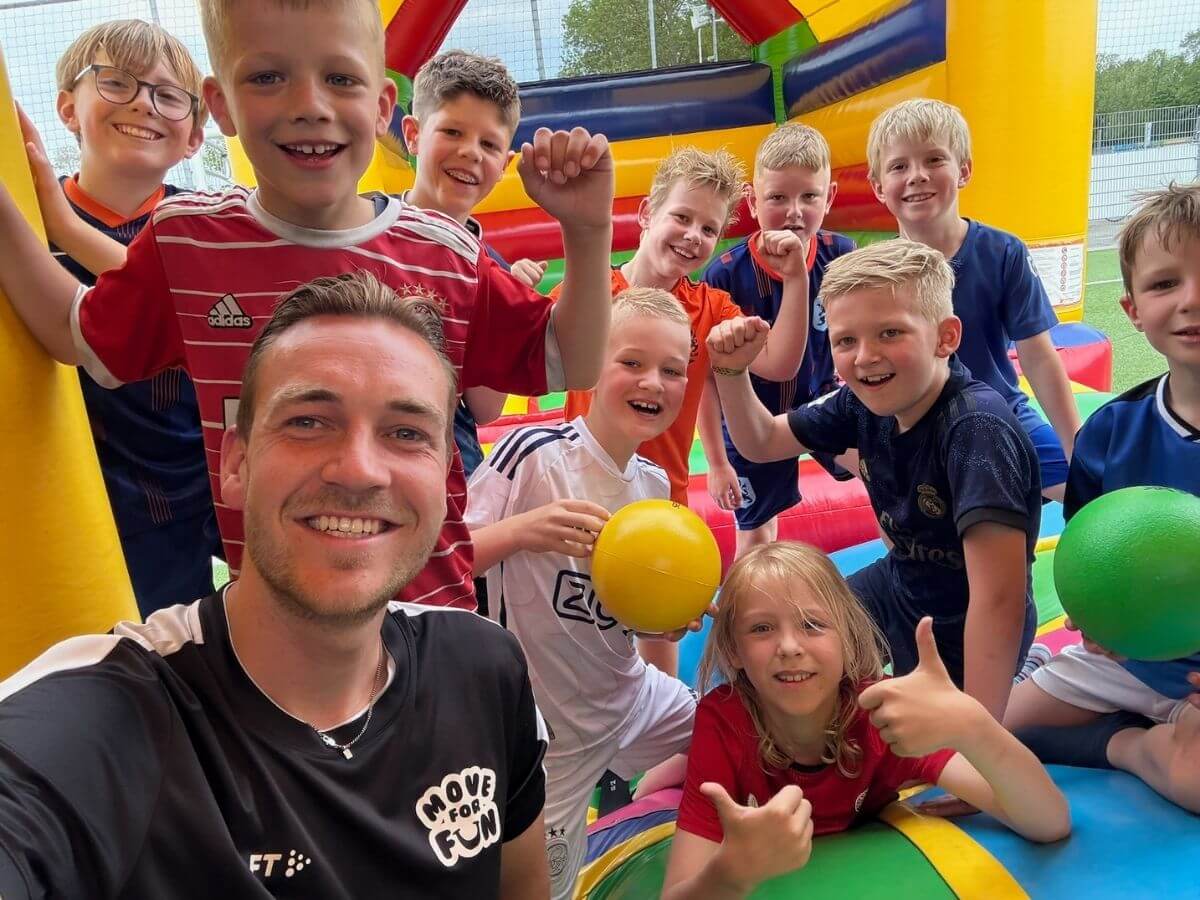Kinderen lachen en poseren samen met een Move For Fun begeleider op een springkussen tijdens Vakantie Fun.