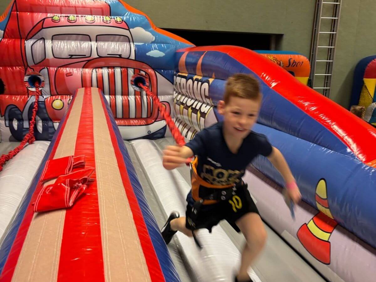 Kind rent over de bungee run tijdens een sport- en speldag met opblaasbare attracties van Move For Fun