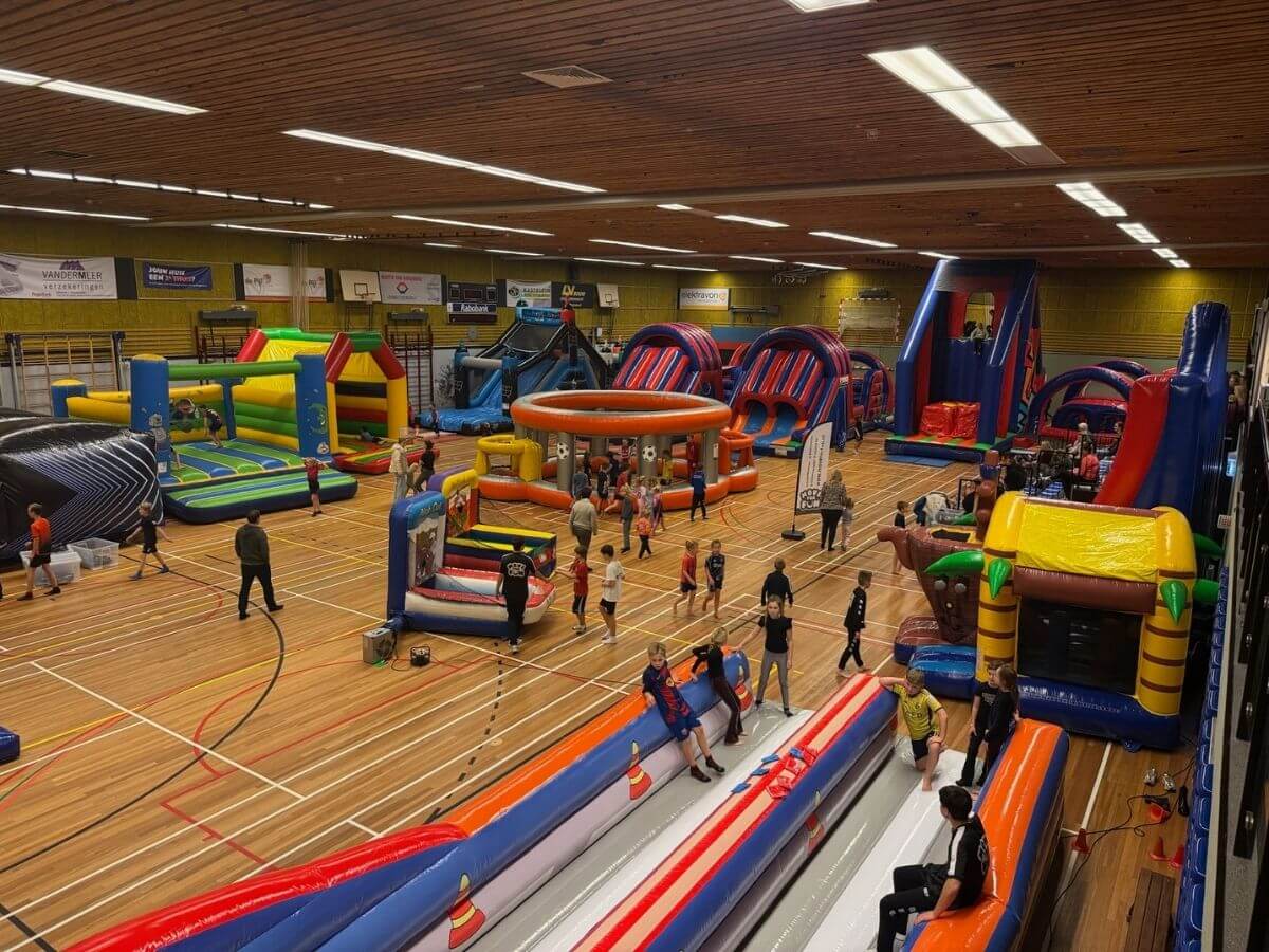 Kinderen spelen op stormbanen en springkussens tijdens een sport- en speldag van Move For Fun in een sporthal